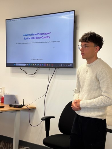 You man standing presenting beside large screen