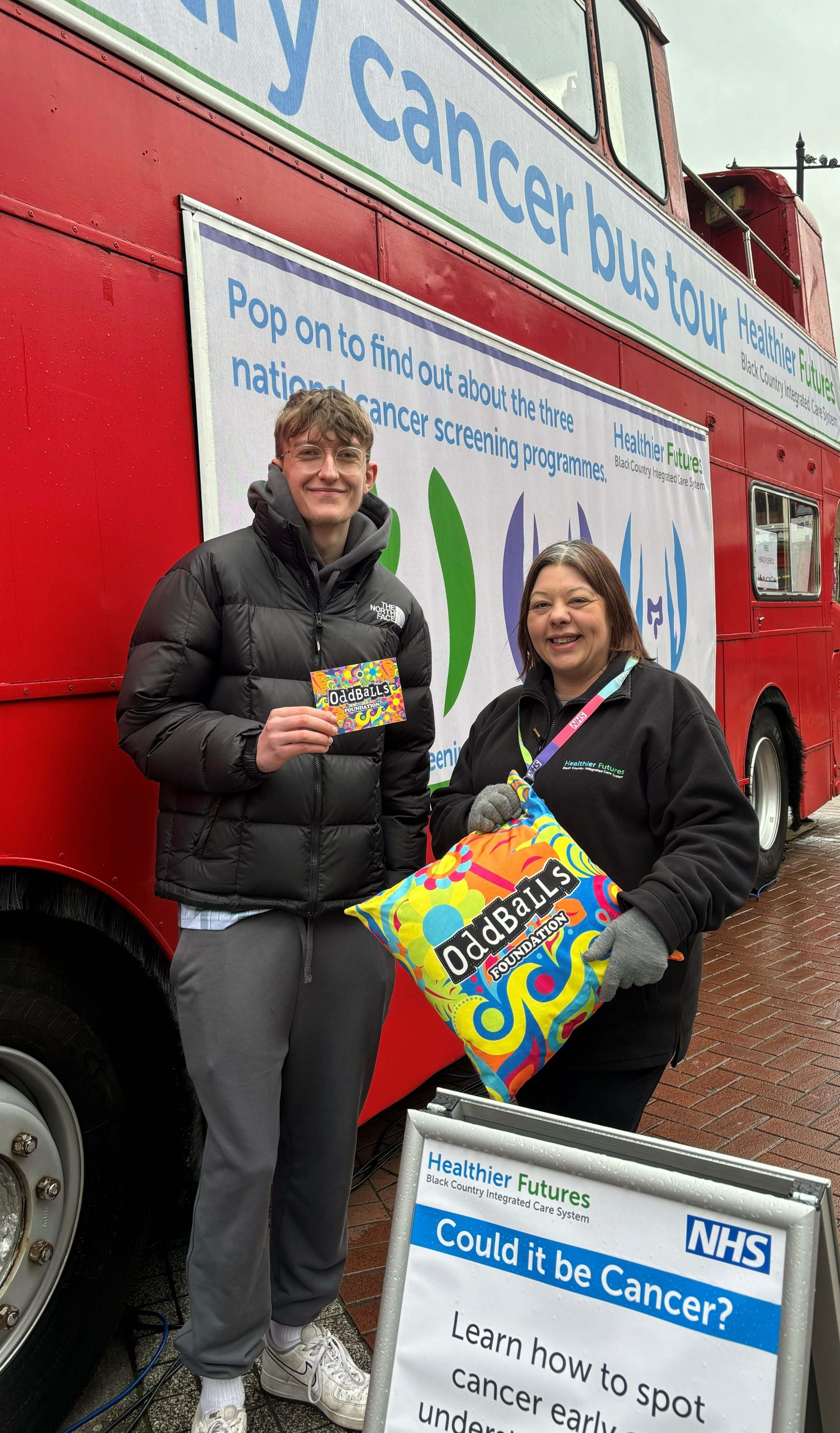 Two people standing in front of double decker cancer bus