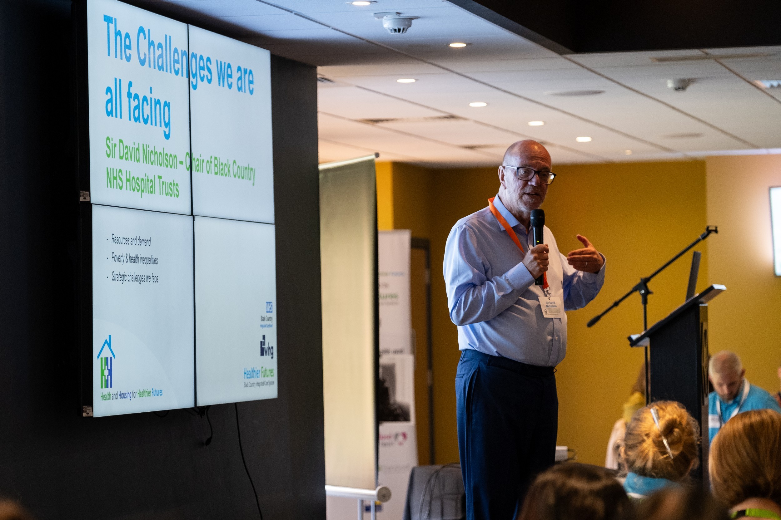 Man standing speaking into microphone in front of image of presentation slides